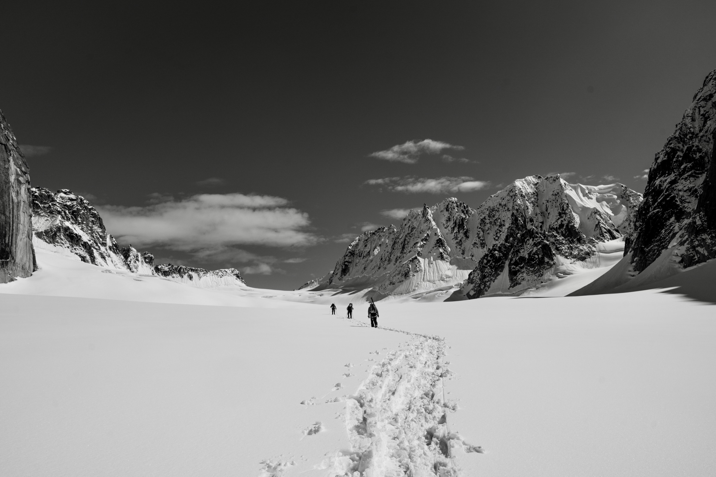 Three skiers breaking trail across an Alaskan glacier toward distant peaks